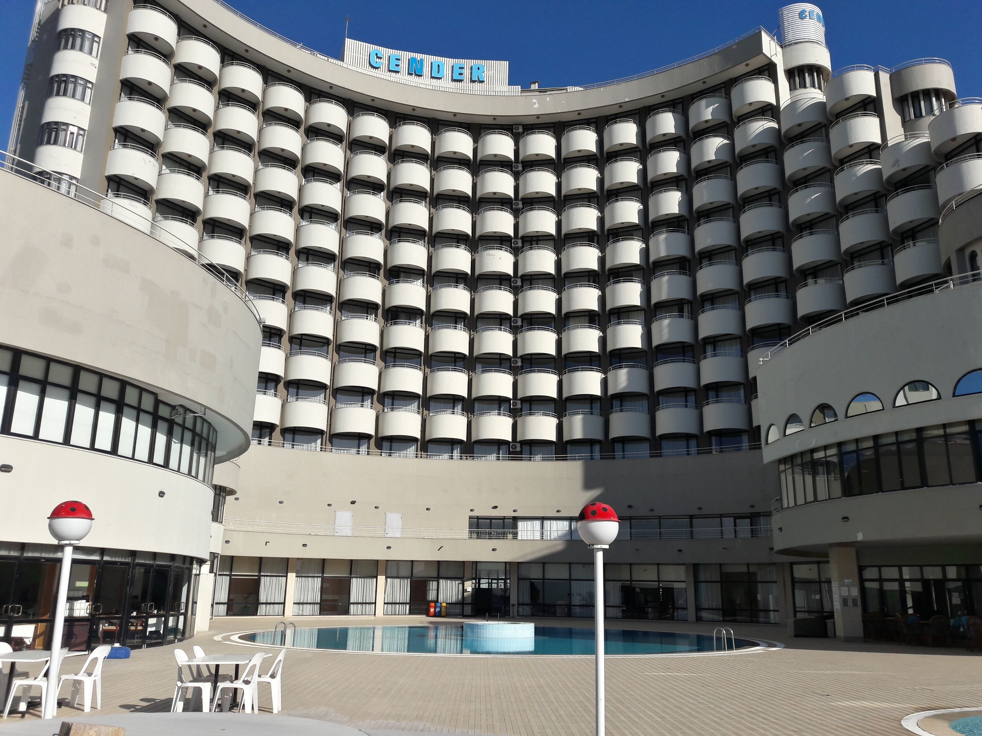 A hotel with a curved facade, multiple balconies, a swimming pool, and outdoor seating areas.