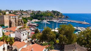 A coastal town with historic buildings, a marina with boats, and a fort overlooking the sea. - Cender Hotel (Antalya)