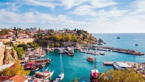 A coastal town with a marina filled with boats, a historic fort, and buildings on a hillside. - Cender Hotel (Antalya)
