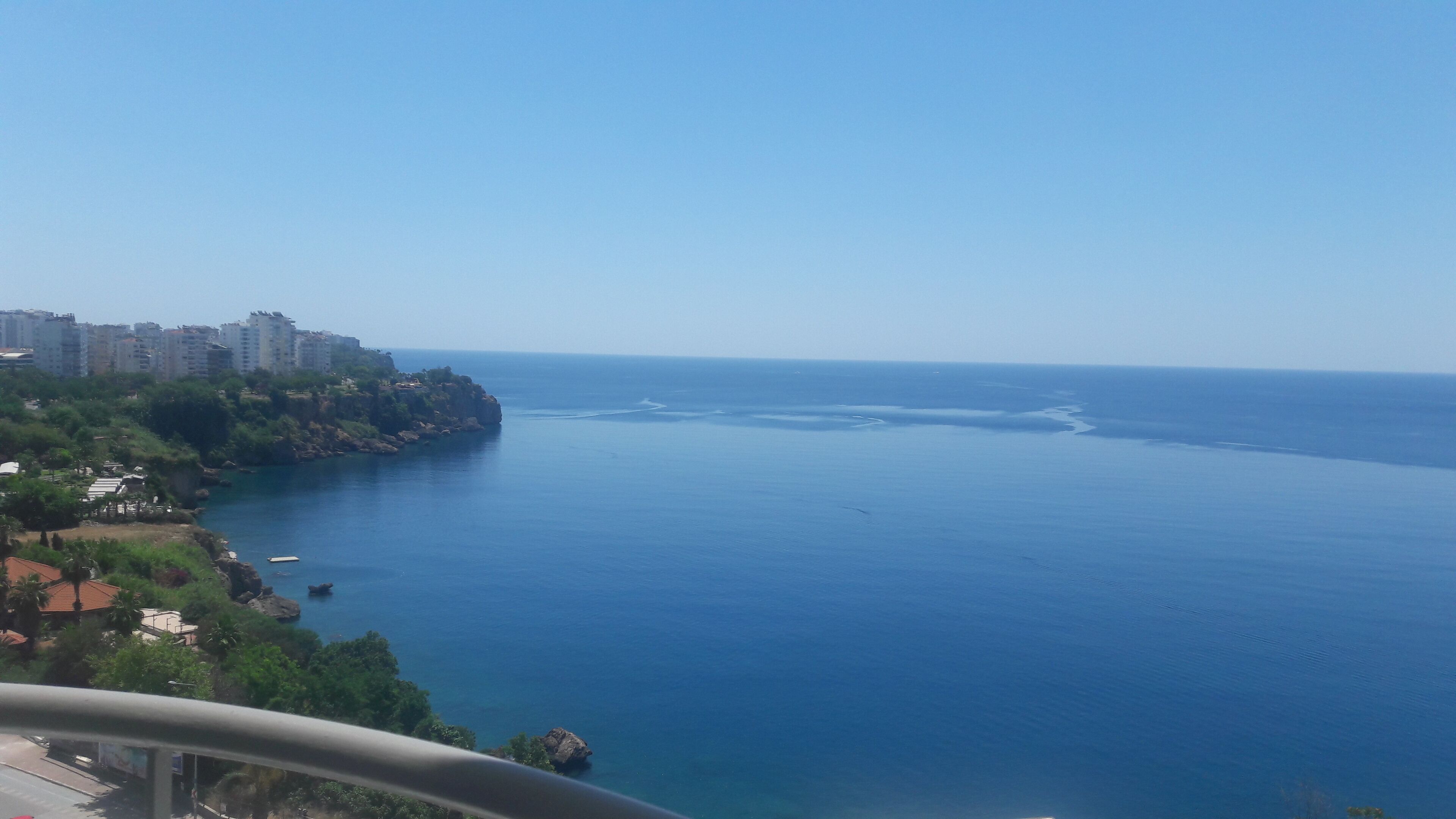 A coastal view with a clear sky, a calm sea, and a rocky coastline with buildings.