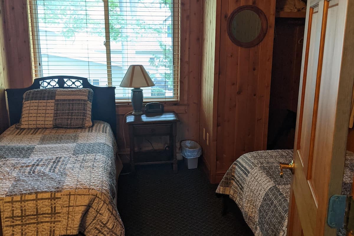Une chambre confortable dans un chalet, avec deux lits, une petite table avec une lampe, une fenêtre avec des stores et une porte.