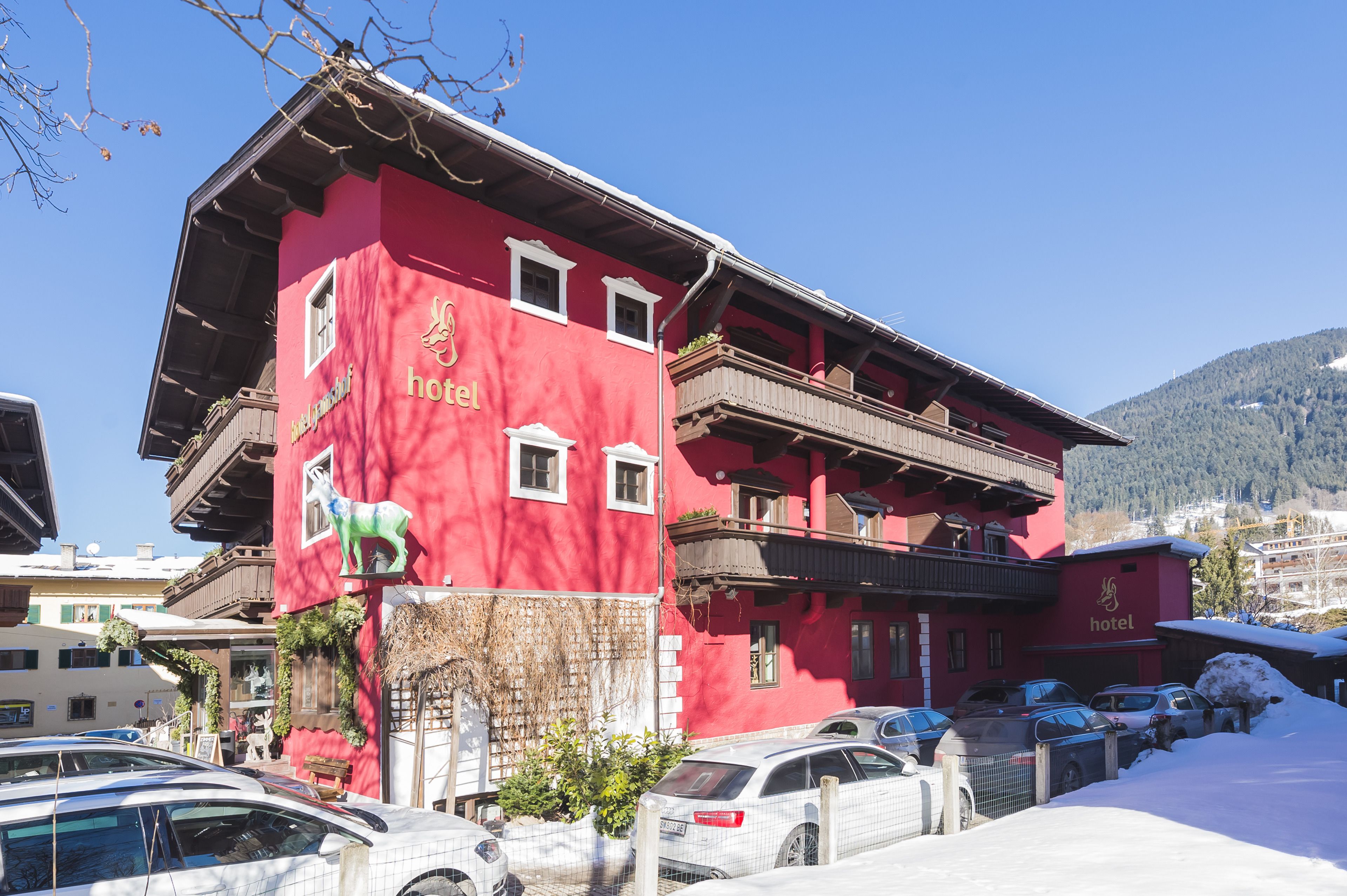 Un edificio de hotel rojo con balcones y un cartel que indica que es un hotel. Hay coches aparcados delante y nieve en el suelo.