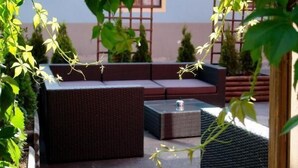 An outdoor seating area with wicker furniture and a small table, surrounded by greenery and a building in the background. - Hotel Gamshof (Kitzbuhel)
