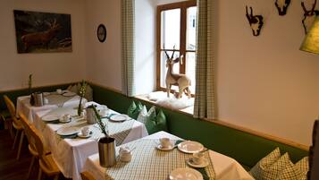 A dining area with checkered tablecloths, wooden chairs, and a view of deer through a window.