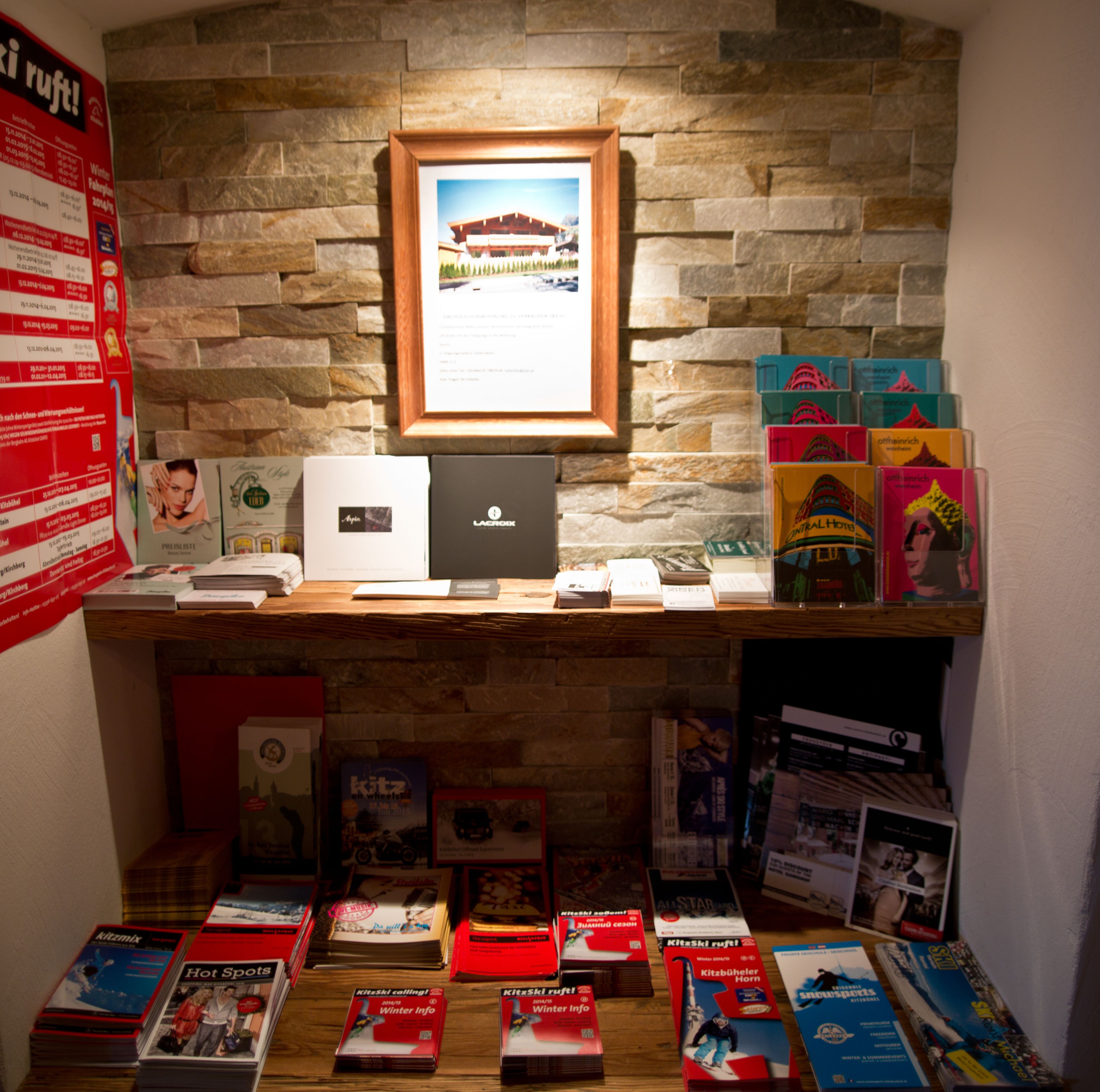 A display of books and magazines on a wooden table with a stone wall background.