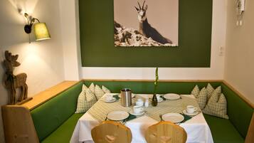 A dining area with a green booth seating, a table set with plates, cups, and a vase with a plant.