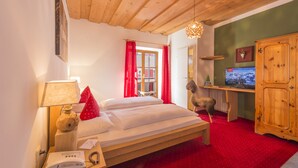 A room with a wooden bed, a desk with a computer, a red carpet, and a wooden ceiling. - Hotel Gamshof (Kitzbuhel)