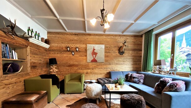 A cozy living room with a wooden wall, a sofa, a coffee table, and a fireplace. - Hotel Gamshof (Kitzbuhel)