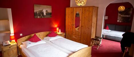 A bedroom with a wooden bed, red walls, a wooden wardrobe, and a small table with a lamp.