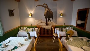 A restaurant with a central table featuring a mounted animal head, surrounded by booths and tables with white tablecloths and wooden chairs. - Hotel Gamshof (Kitzbuhel)