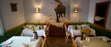 A restaurant with a central table featuring a mounted animal head, surrounded by booths and tables with white tablecloths and wooden chairs.