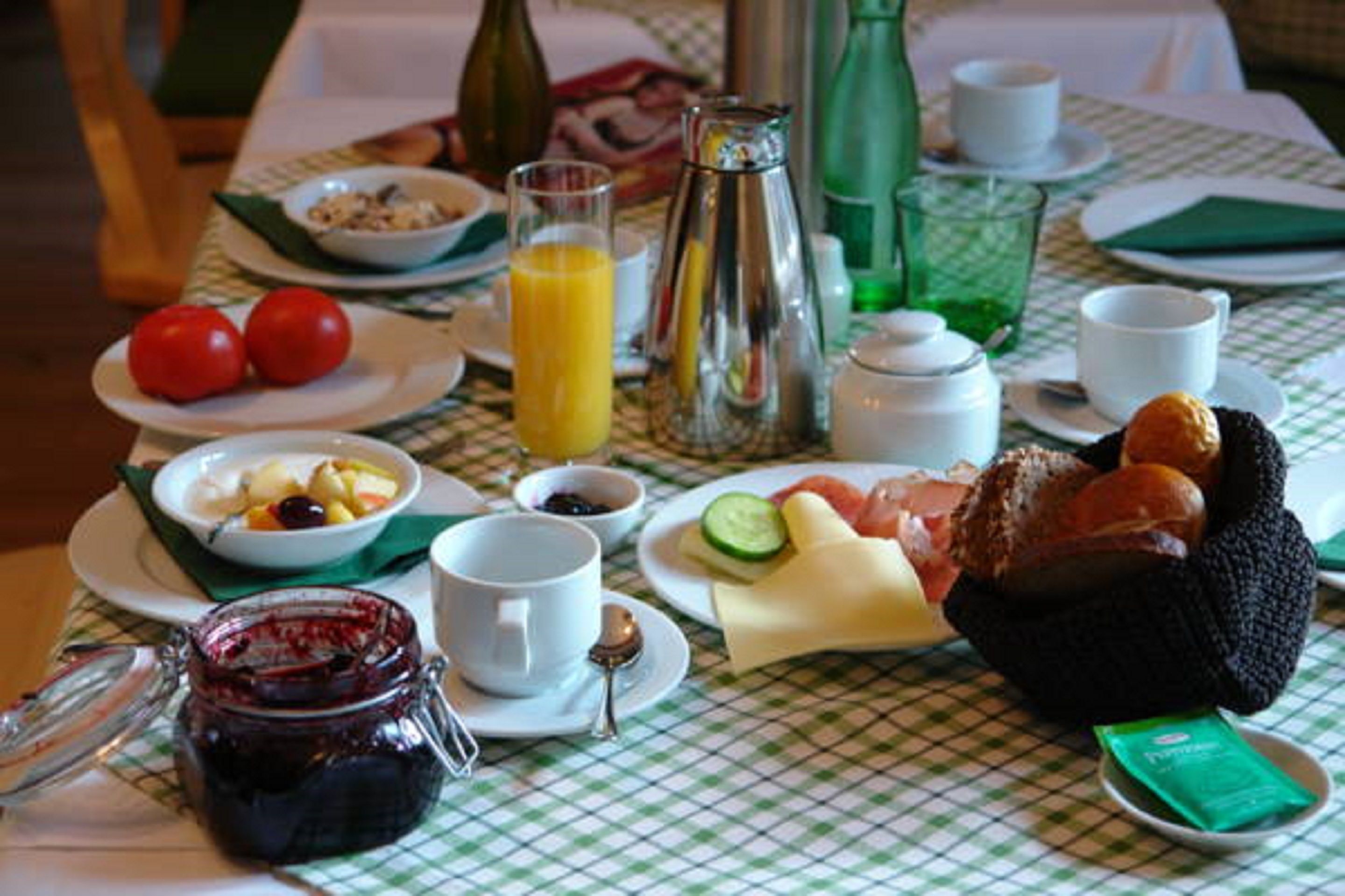 A breakfast table with various dishes, including bread, tomatoes, and a jug of juice.