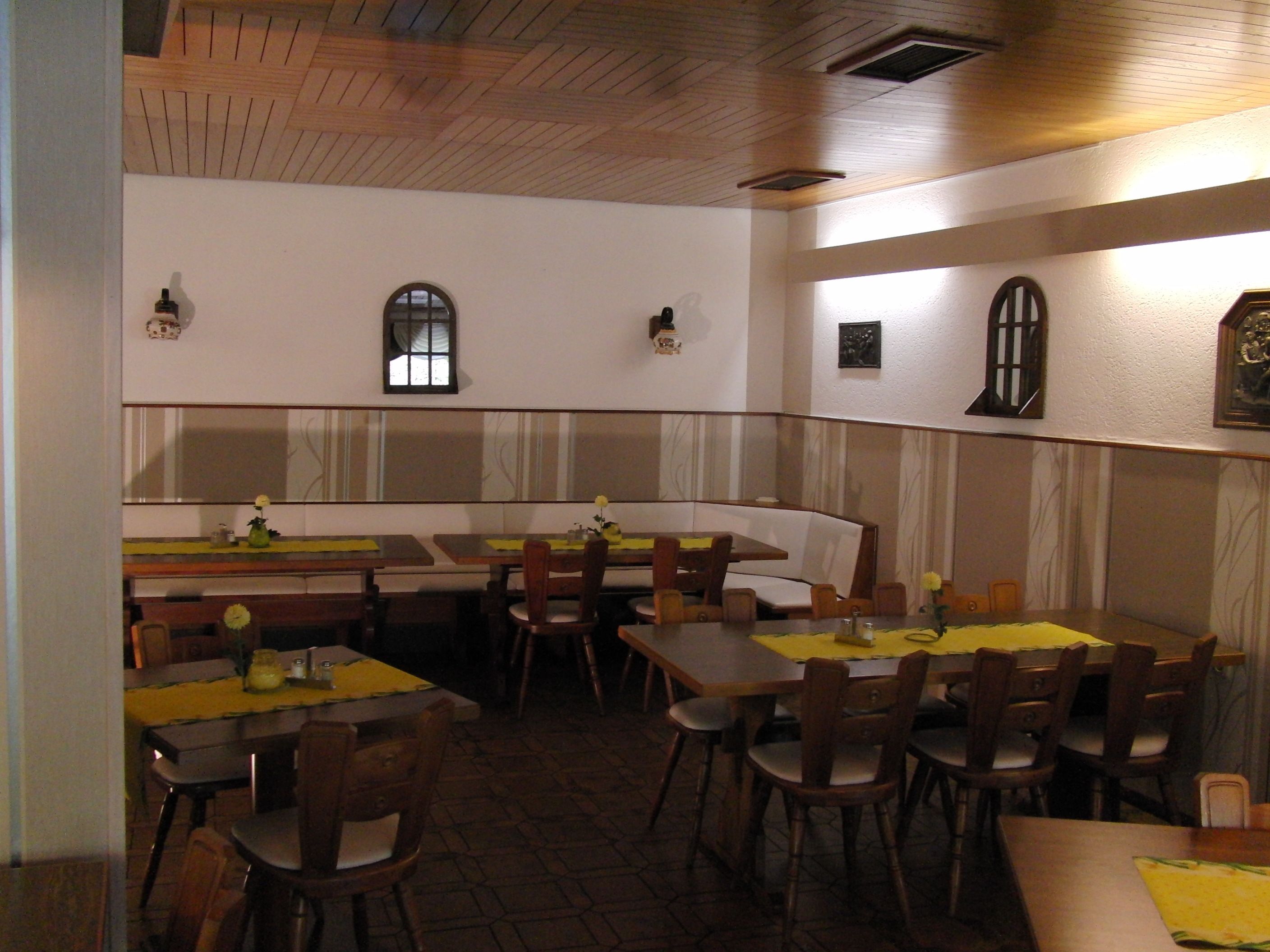 A restaurant with booths and tables, wooden ceiling, and wall-mounted lights.