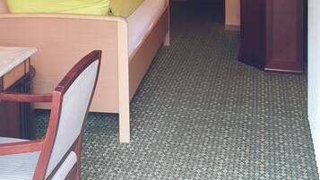 A small, single-room hotel room with a bed, a desk, a chair, a television, and a radiator.