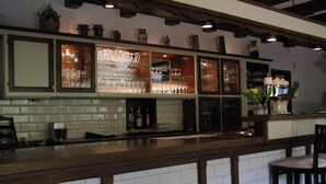 Zona de bar con un rebozo de azulejos, estantes con copas y mostrador de madera.