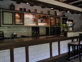 Uma área de bar com painel de azulejos, prateleiras com copos e balcão de madeira.