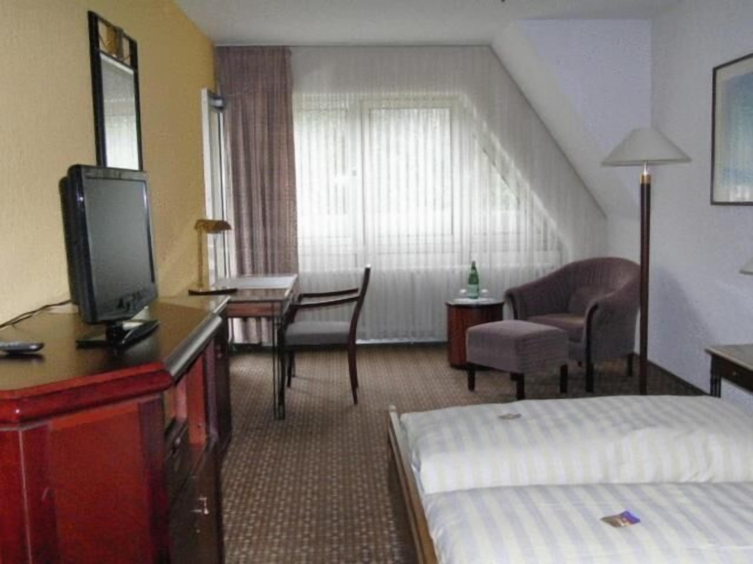A hotel room with a bed, a desk with a chair, a television, and a lamp.