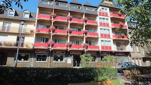 Un hotel de varios pisos con balcones decorados con cestas de flores, un restaurante y una cafetería.