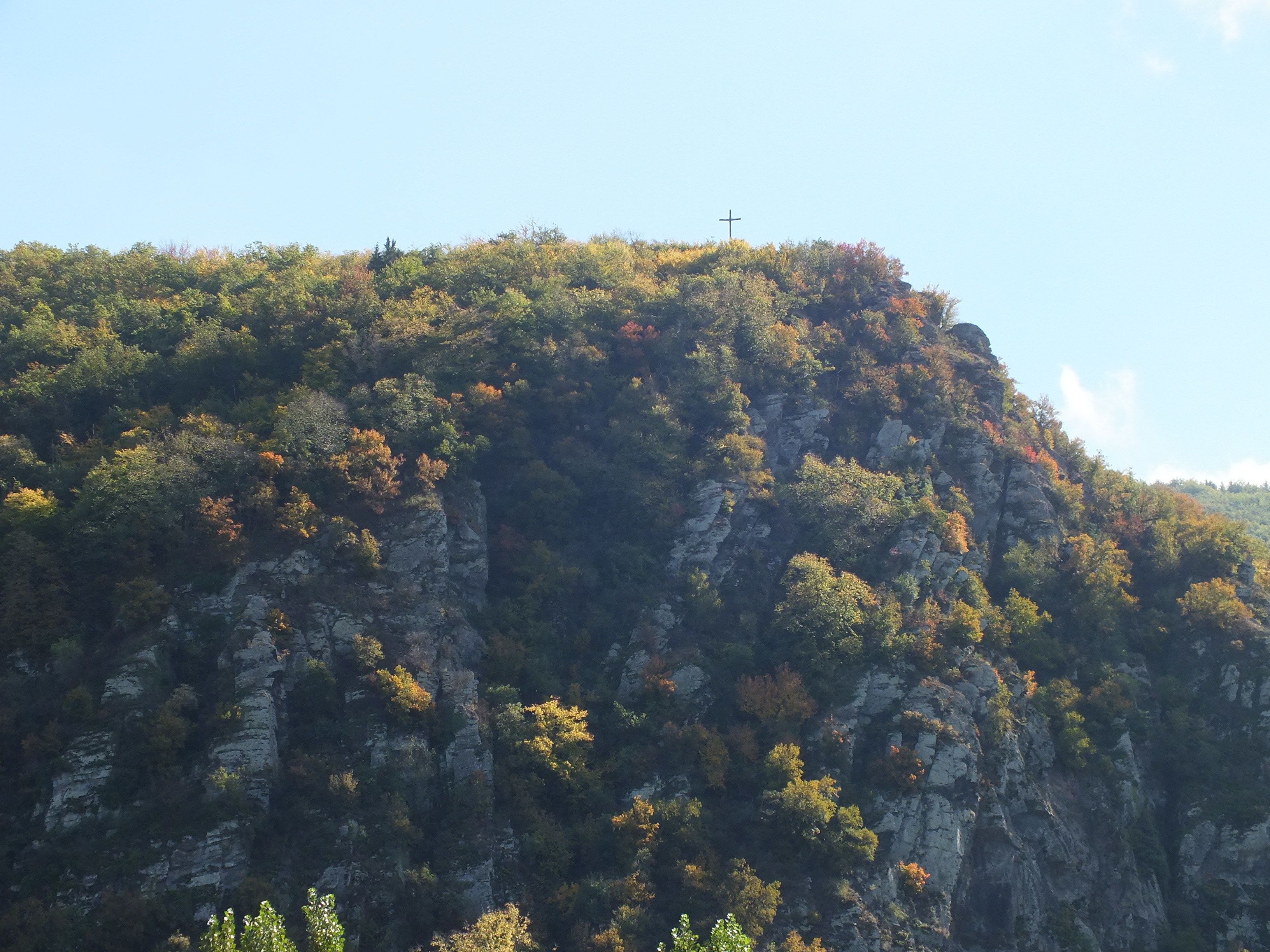 Een bergachtig landschap met een kruis bovenop, weelderige begroeiing en rotsachtige kliffen.