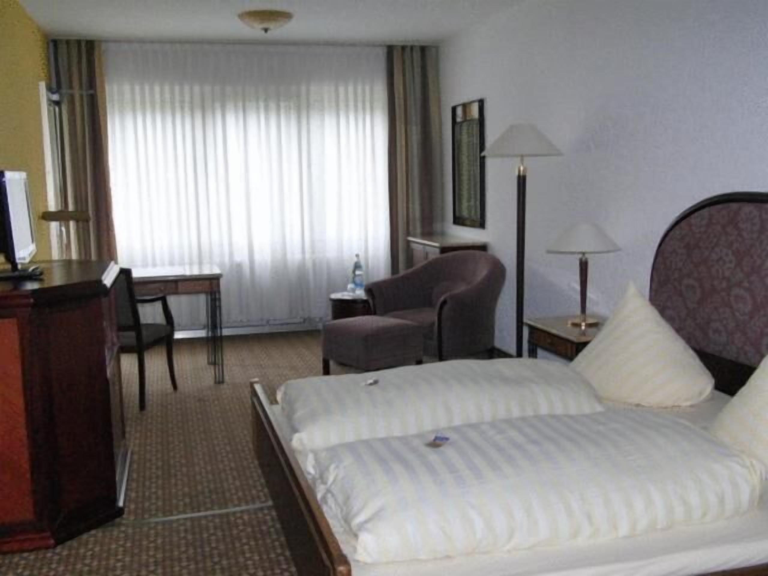 A hotel room with a bed, a desk, a chair, a lamp, and a television.