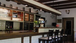 Una zona de bar con mostrador de madera, varios taburetes y estanterías con copas y botellas.