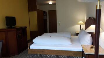 Habitació d'hotel amb llit, taulella, làmpada, televisió i armari.