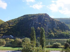 A view of a mountain with a church on top, a river in the foreground, and a road with a car. - Hotel Moselkern (Moselkern)