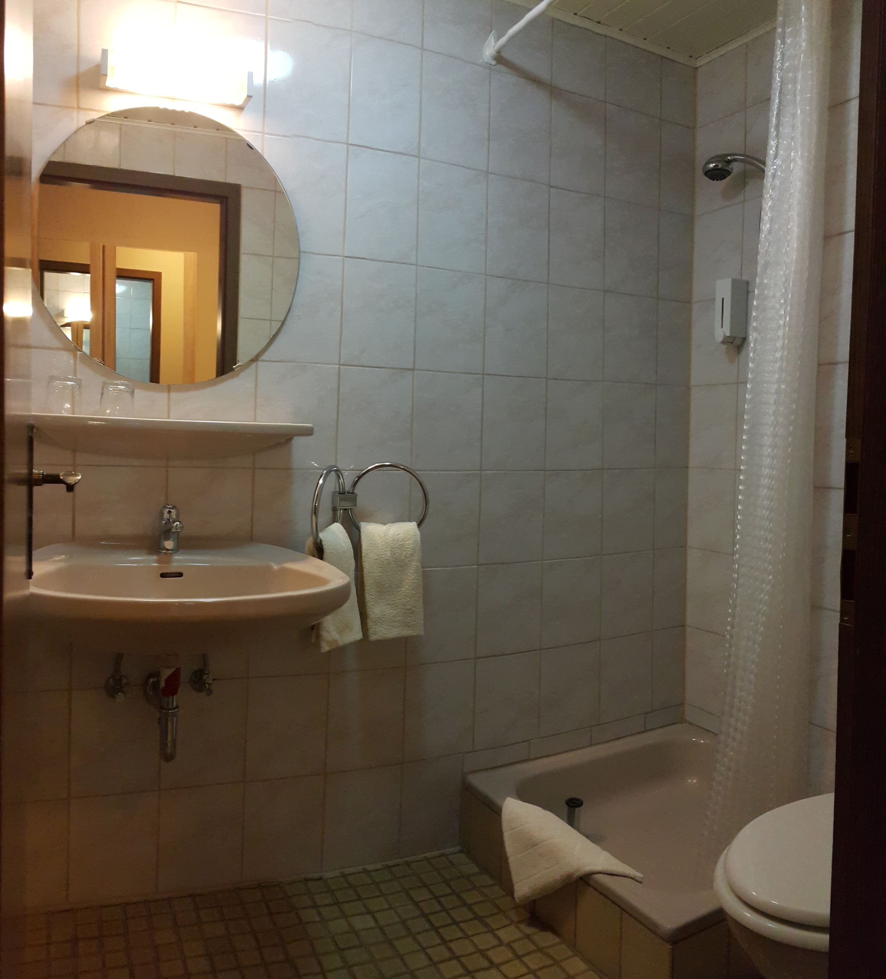 Een badkamer met een wastafel, spiegel, handdoekhouder, toilet en bad.