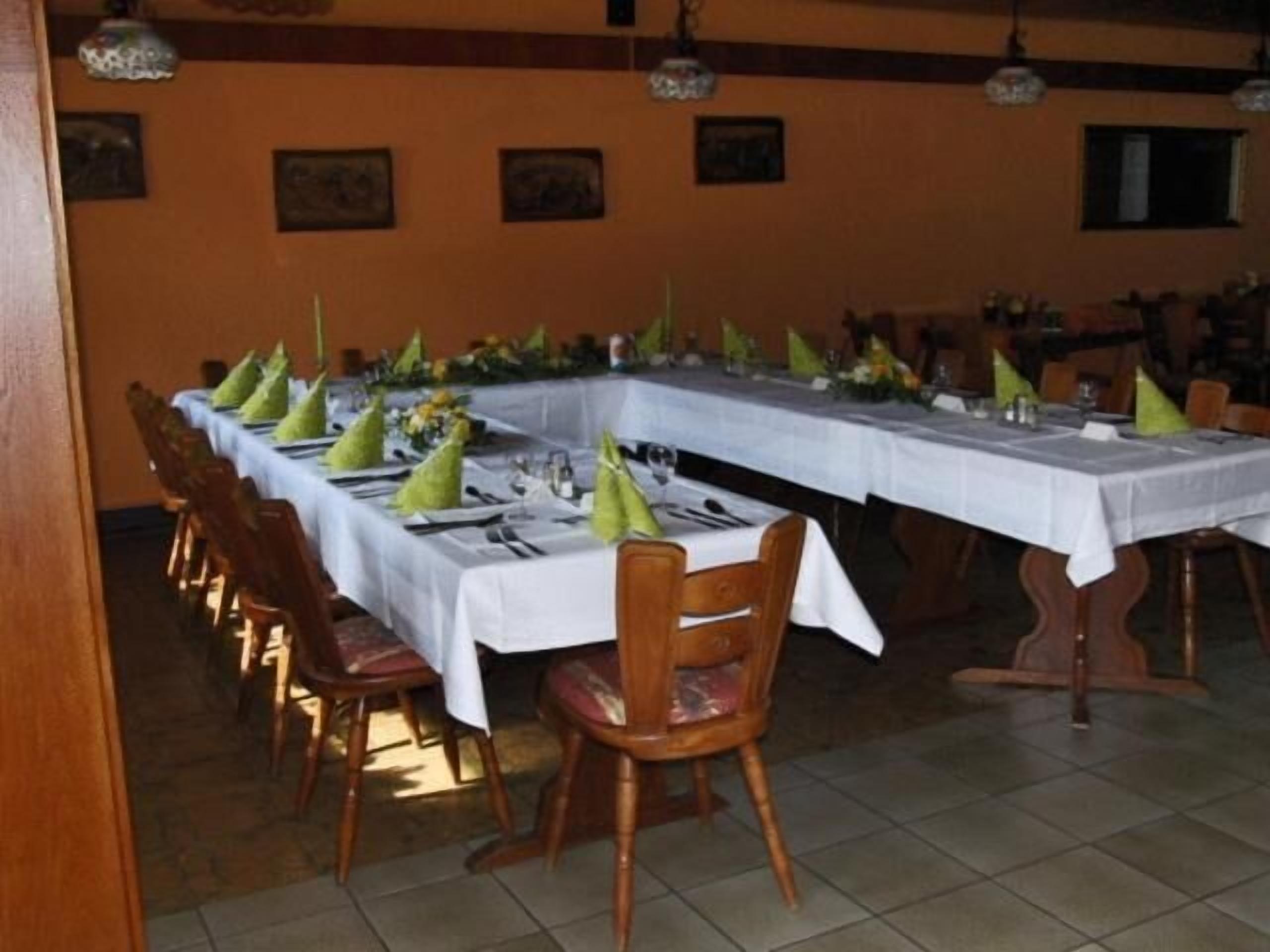 Un espace repas avec de longues tables disposées pour accueillir plusieurs convives, des chaises en bois et un sol carrelé.