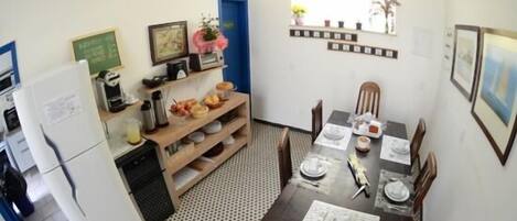 Cocina compacta con refrigerador, pileta y estantes de madera. Mesa de comedor con sillas dispuesta para cuatro.