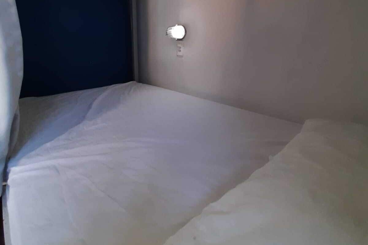 Uma cama de solteiro num quarto com parede azul e luminária na parede.