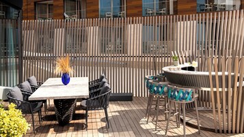 Eine Terrasse im Freien mit Tisch und Stühlen, einer dekorativen Vase und einem kleinen runden Tisch mit einem Getränk.
