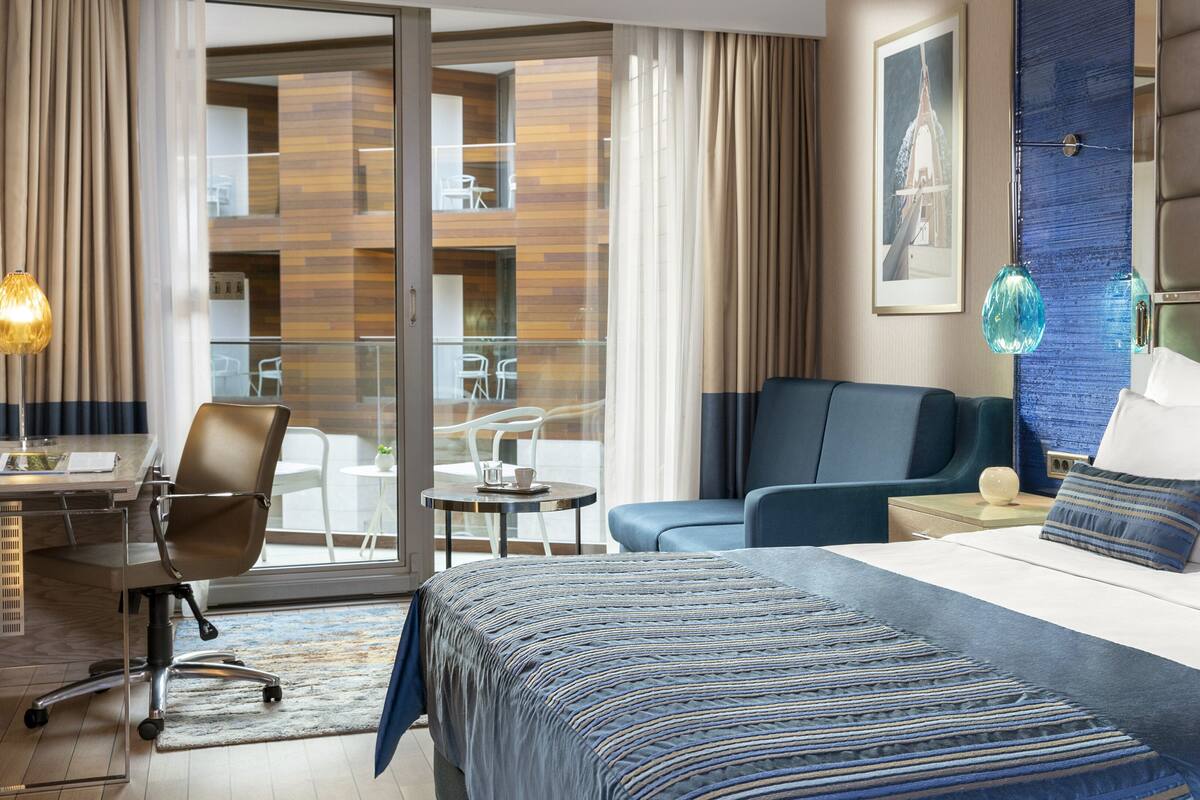 A hotel room with a bed, a desk, a chair, and a view of the outside.