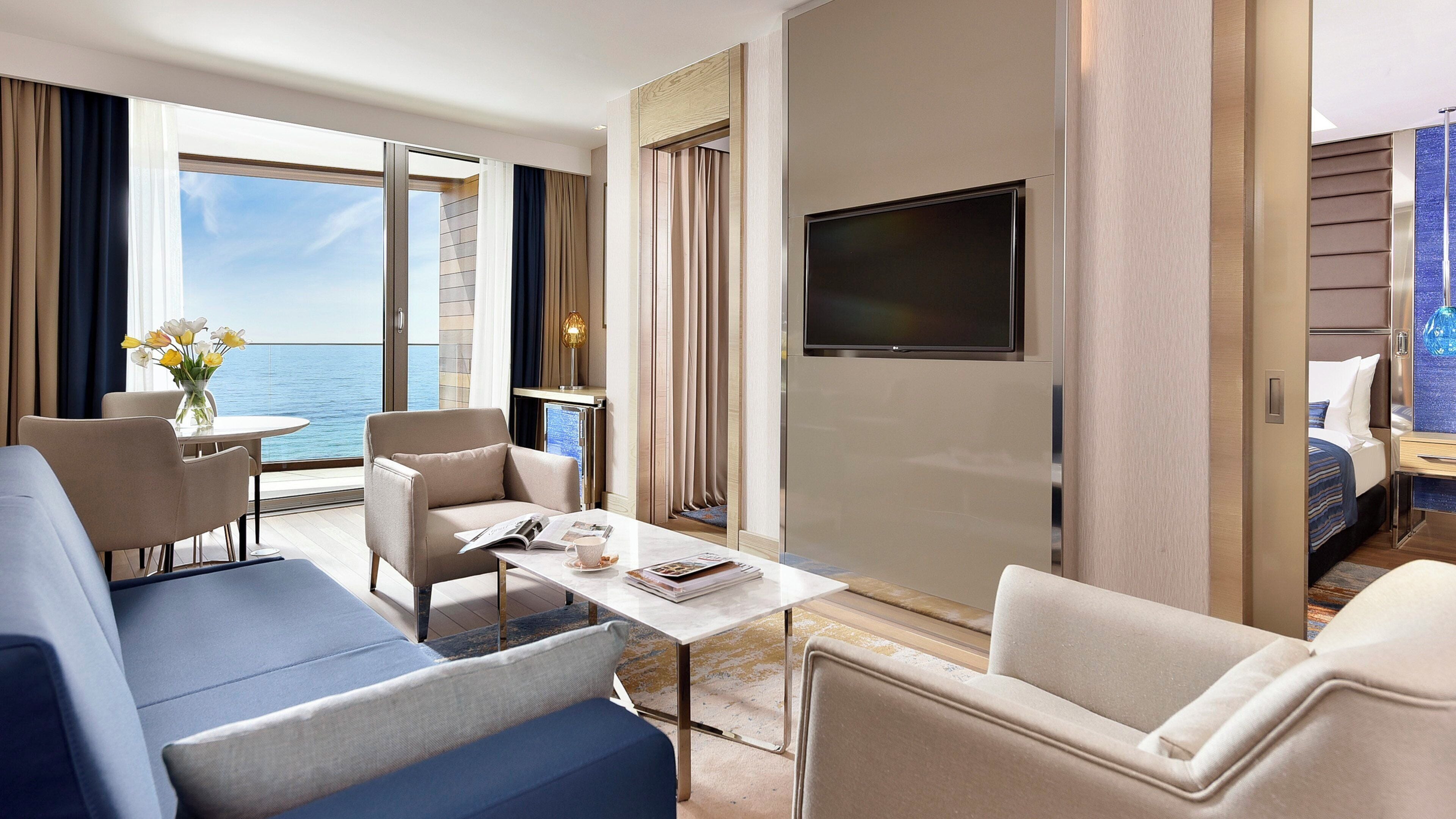 A hotel room with a balcony, a flat-screen TV, a sofa, a coffee table, and a bed.