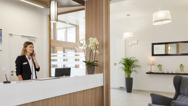 Un comptoir d’accueil au design moderne, une plante en pot, un espace détente avec un fauteuil et un grand miroir mural.