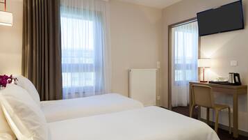 Habitación de hotel con dos camas, un escritorio con silla, un televisor montado en la pared y una ventana con cortinas.