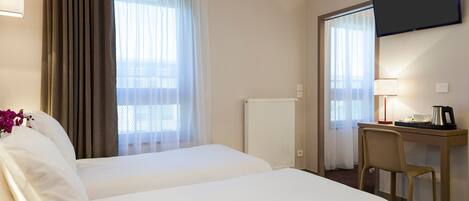 A hotel room with two beds, a desk with a chair, a TV mounted on the wall, and a window with curtains.
