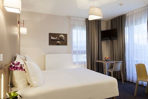 Habitación de hotel con cama, escritorio, silla, televisor y ventana con cortinas.