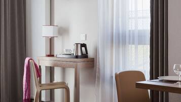 Habitación de hotel con cama, escritorio con lámpara, televisión, silla, mesa con vaso y ventana con cortinas.
