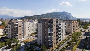 Un immeuble d’appartements moderne, doté de plusieurs étages, de balcons et offrant une vue sur une montagne en arrière-plan.