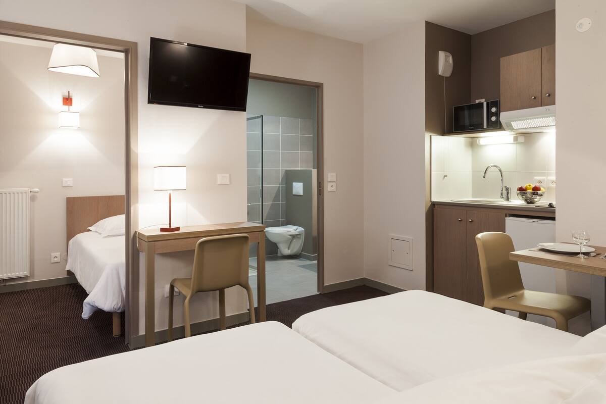 Habitación de hotel con cama, escritorio, silla, televisor y kitchenette equipada con microondas y lavabo.