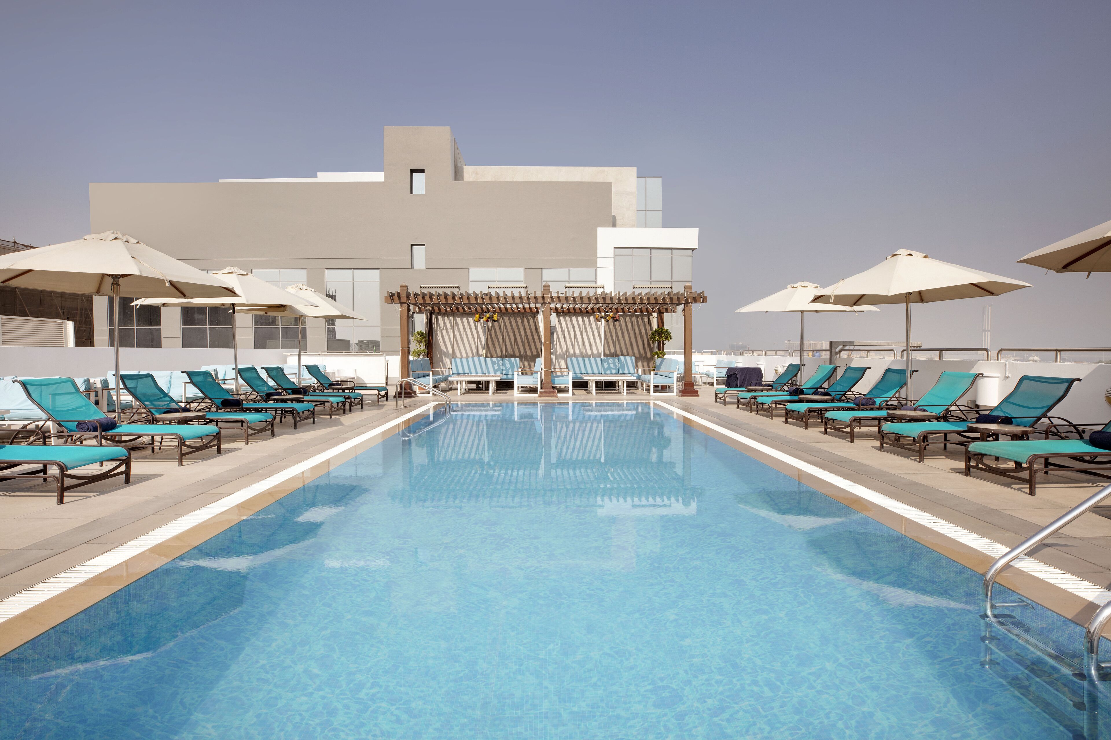 A swimming pool with lounge chairs and umbrellas, surrounded by a modern building.