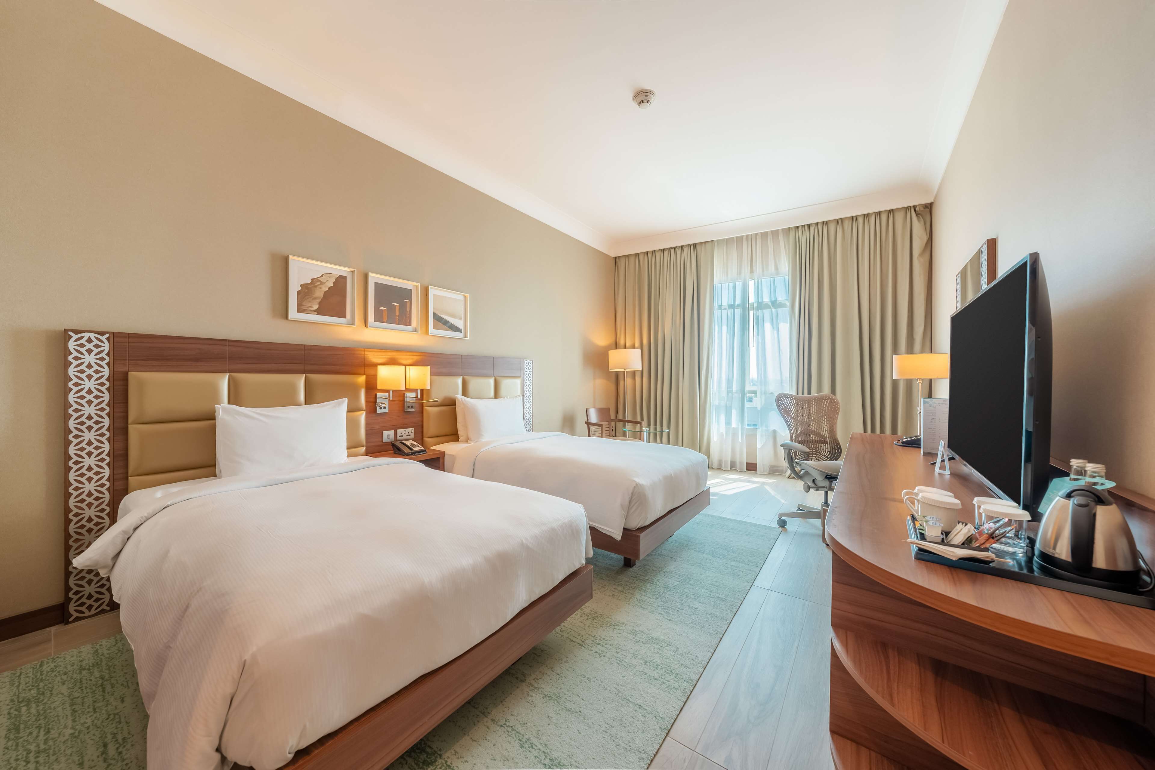 Habitación de hotel con dos camas, un escritorio con televisor y una silla.