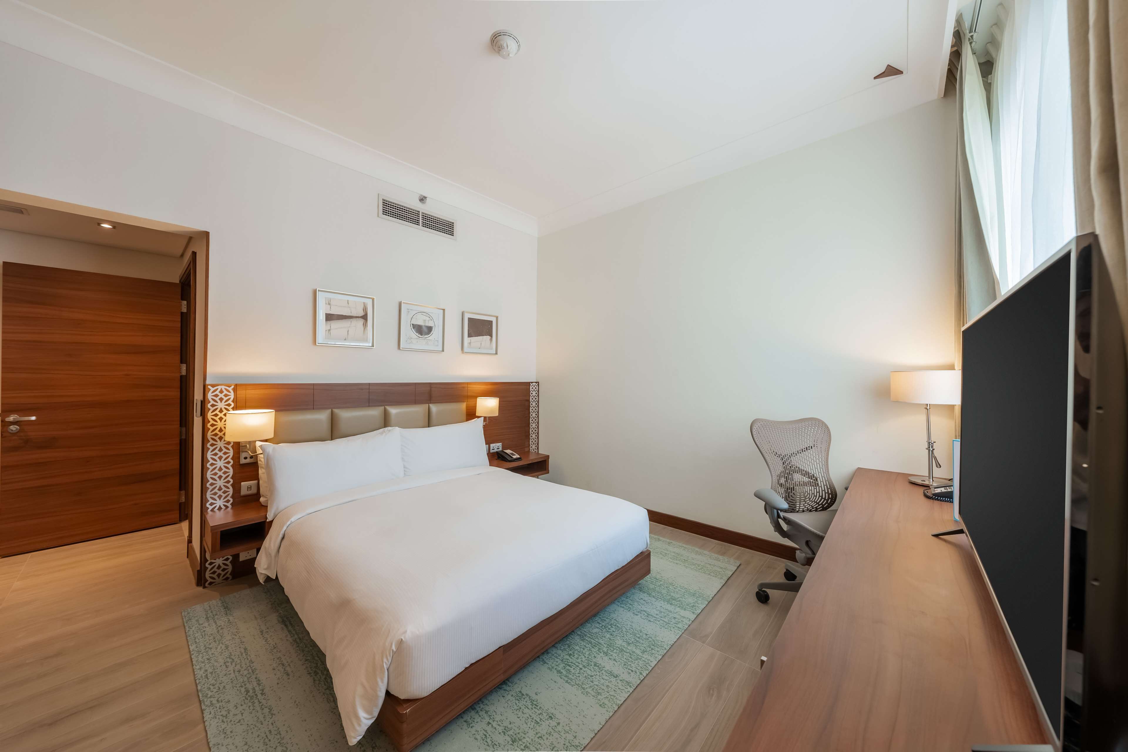 Une chambre d’hôtel avec un grand lit, un bureau, une chaise, une télévision et une armoire.