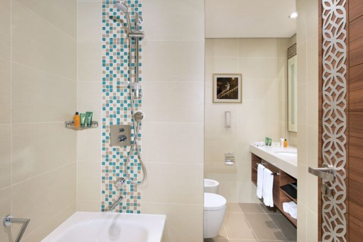 Een moderne badkamer met een douche, een bad en een toilet. Er is een wastafel met een spiegel en een handdoekhouder.