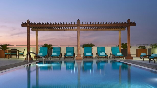Ein Poolbereich mit Holzpergola, Liegestühlen und klarem Wasser.