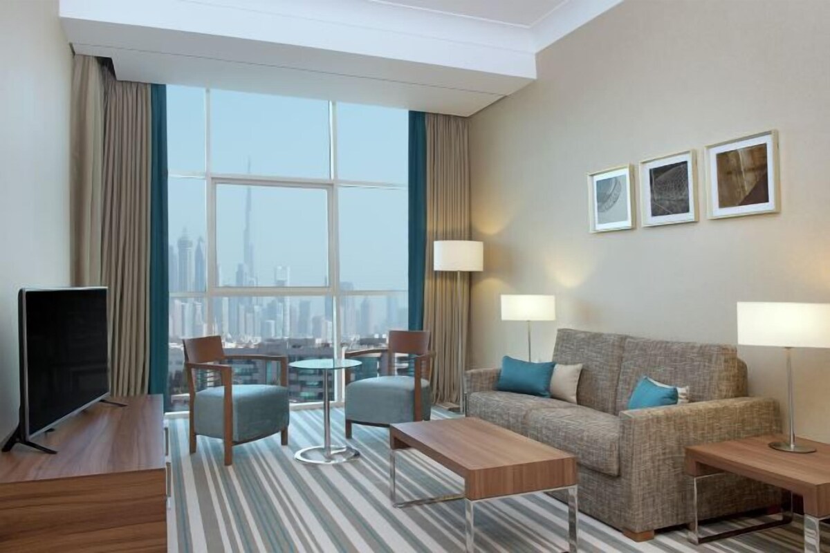 Ein modernes Hotelzimmer mit großem Fenster, einer Couch, einem Couchtisch, einem Fernseher und zwei Lampen.