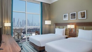 Ein Hotelzimmer mit zwei Betten, einem Schreibtisch, einem Stuhl und Blick auf eine Stadtlandschaft.