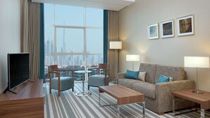 Ein modernes Hotelzimmer mit großem Fenster, einem Flachbildfernseher, einer Couch, zwei Sesseln, einem Couchtisch und zwei Lampen.