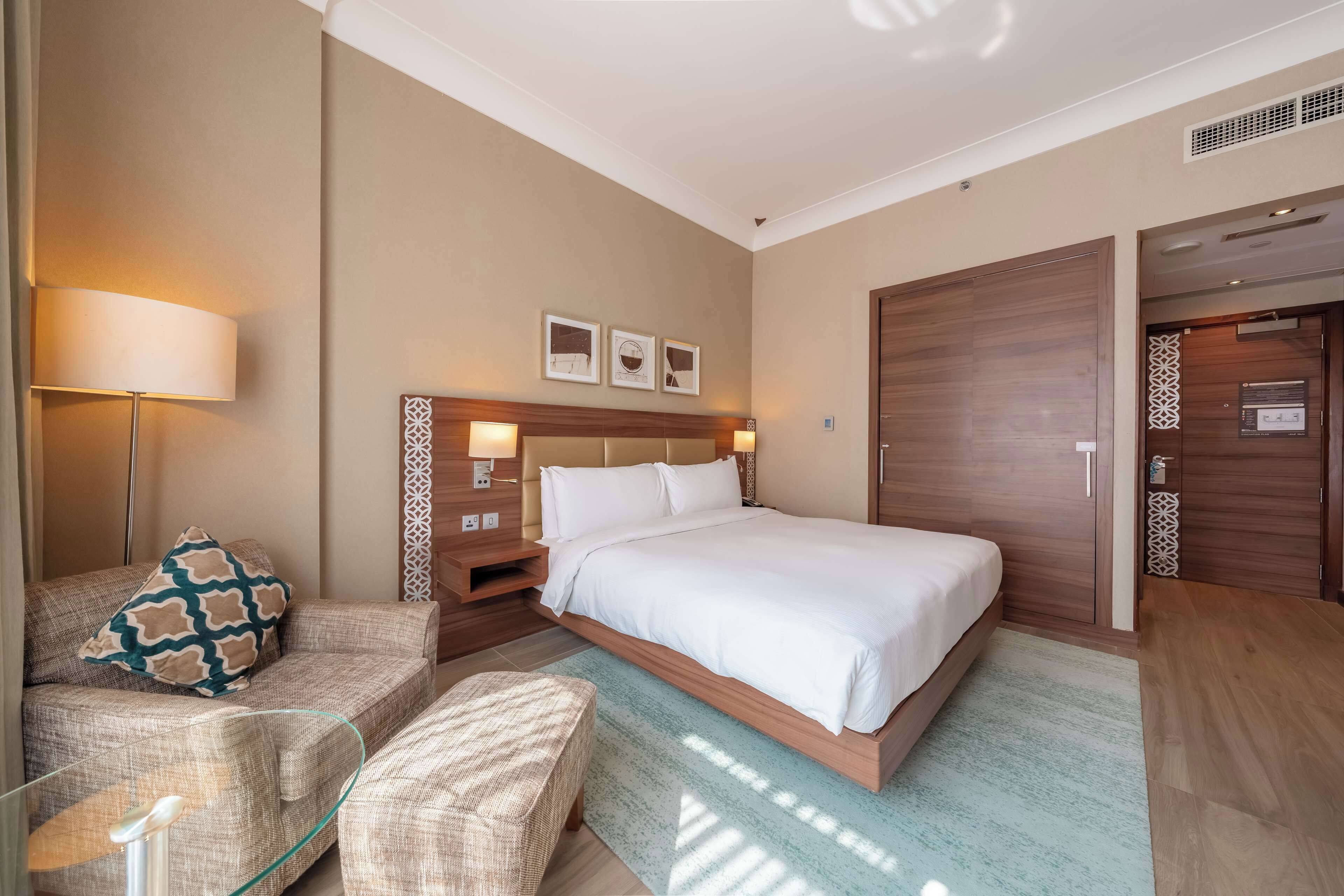 A hotel room with a large bed, a sofa, a bedside table, and a lamp.